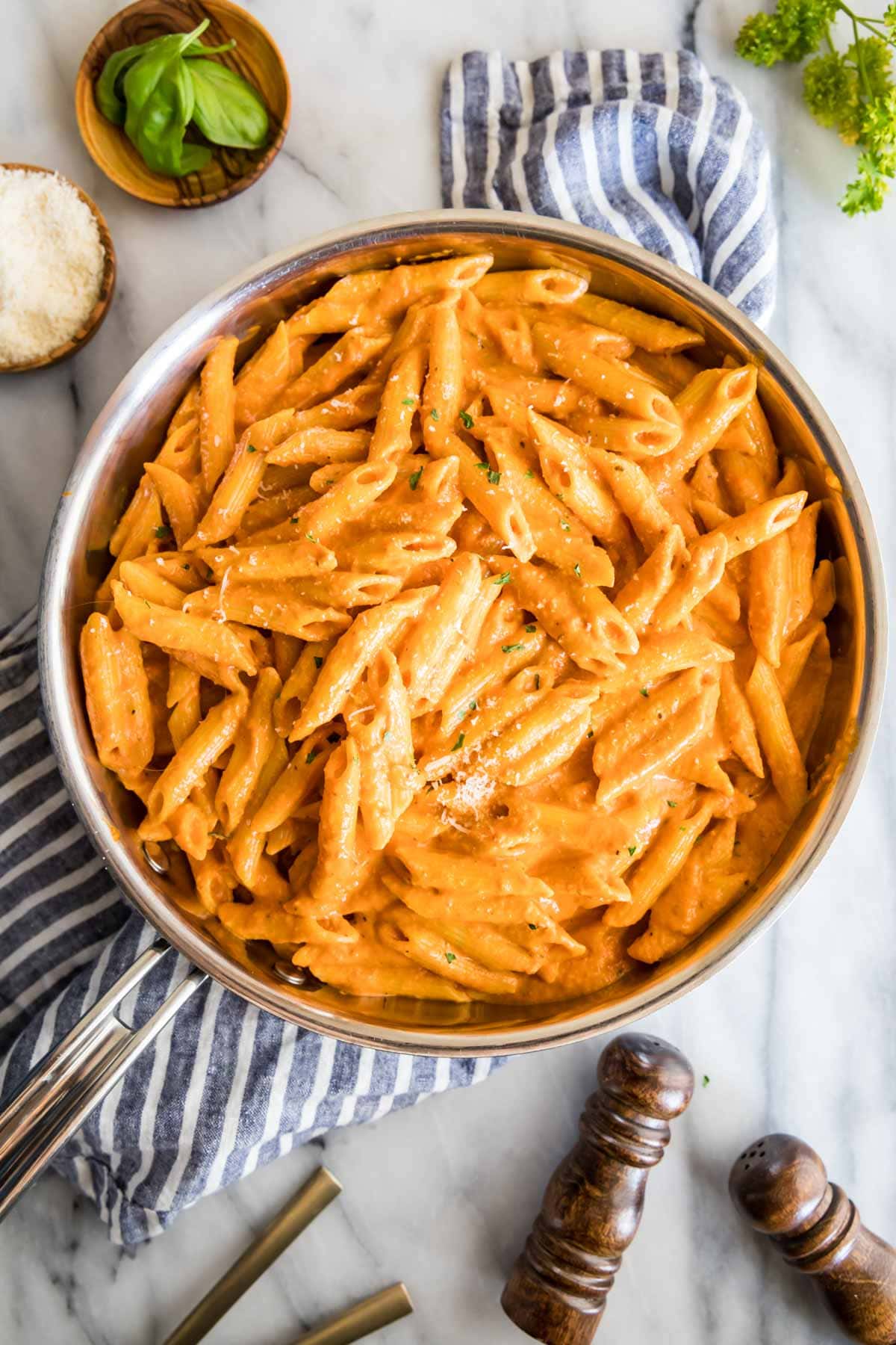 Overhead view of a skillet of penne alla vodka topped with parmesan and fresh basil.