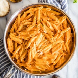 Overhead view of a skillet of penne alla vodka topped with parmesan and fresh basil.