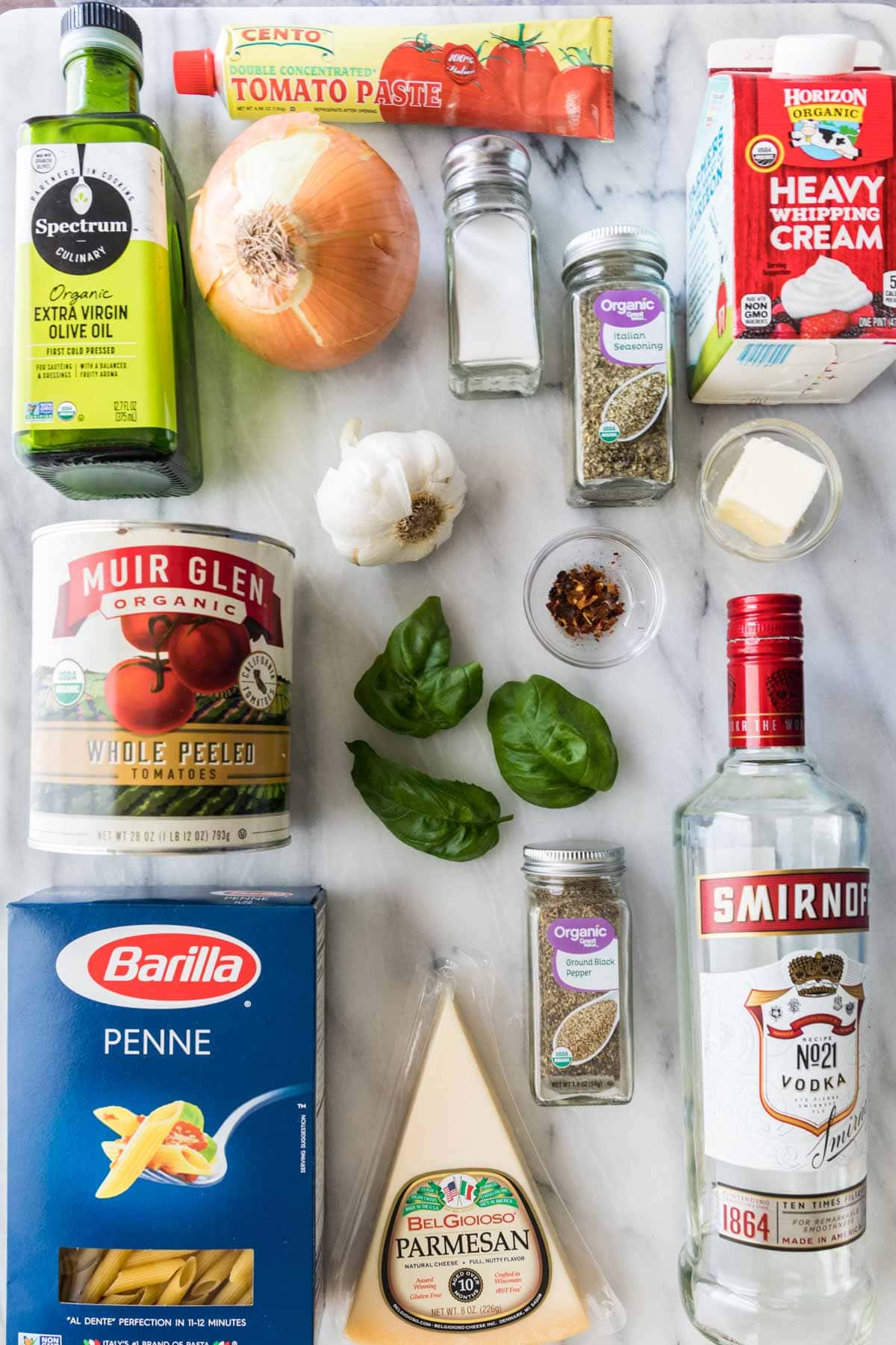 Overhead view of ingredients including penne pasta, vodka, canned tomatoes, cream, and more.