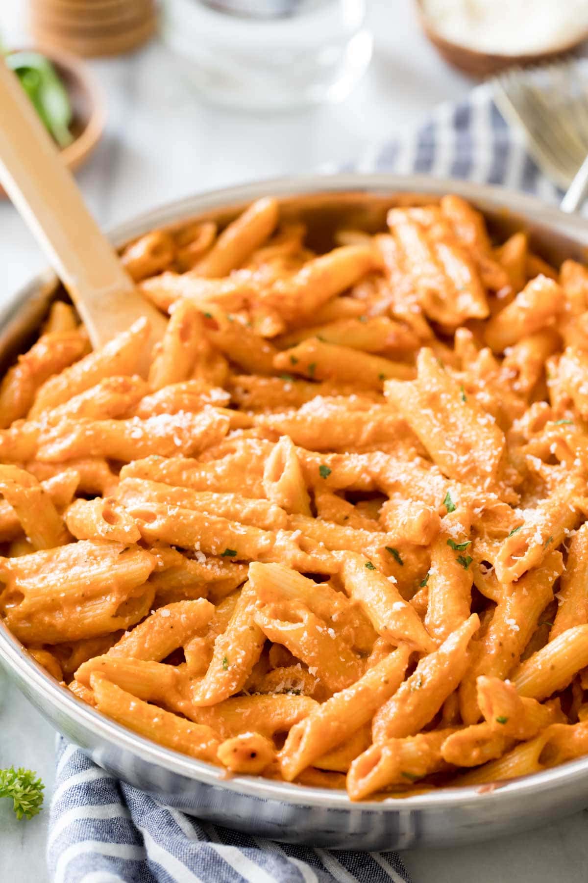 Wooden spoon resting in a large skillet of penne alla vodka topped with parmesan cheese.