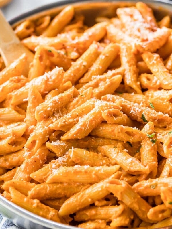 Wooden spoon resting in a large skillet of penne alla vodka topped with parmesan cheese.