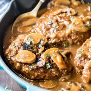 Salisbury steak in a pan with gravy and mushrooms.