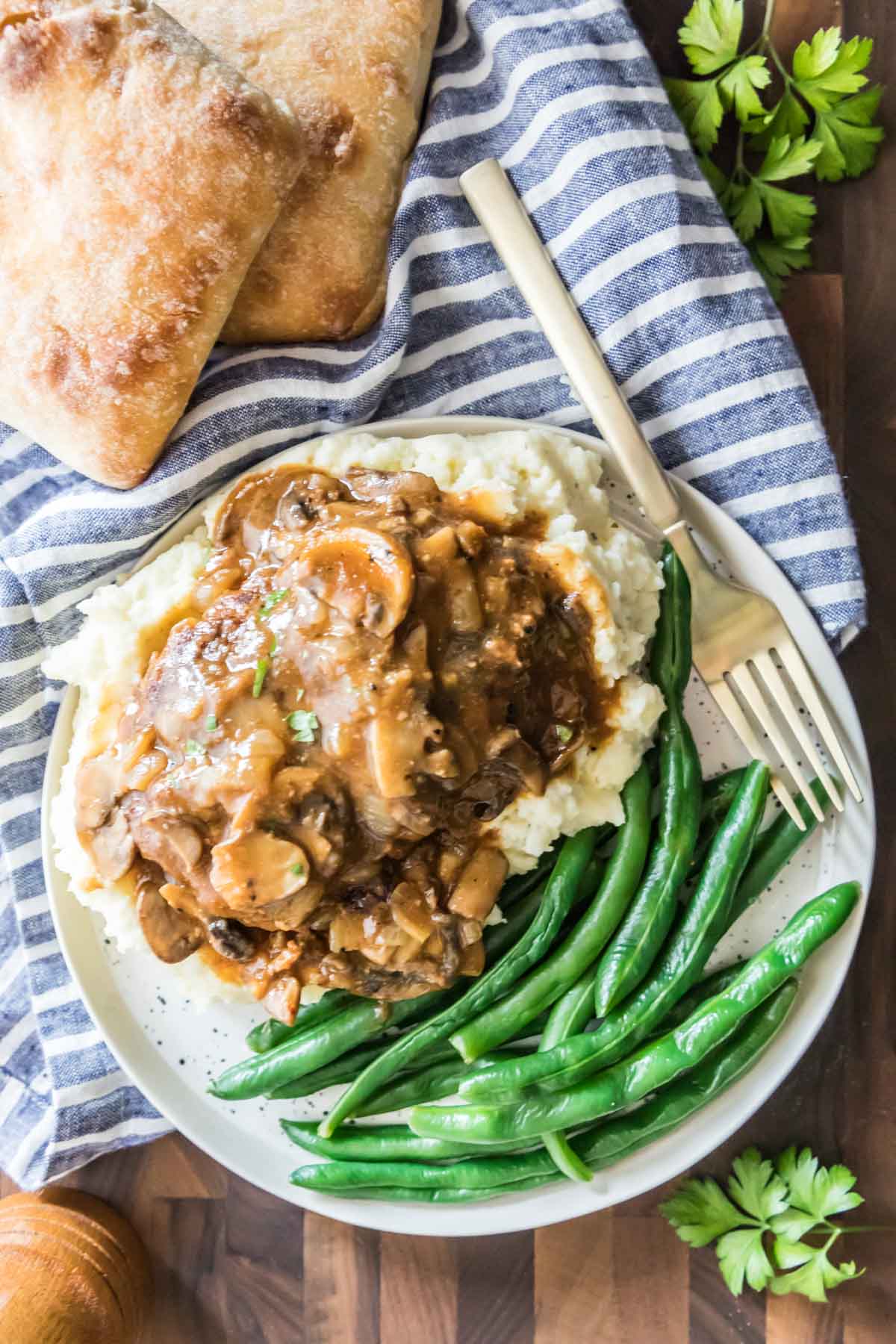 Overhead view of meat and gravy over mashed potatoes served with a side of green beans.