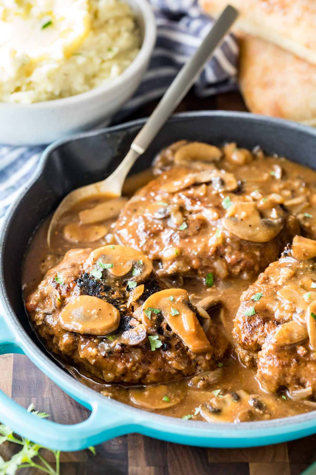 Salisbury steak in a pan with gravy and mushrooms.