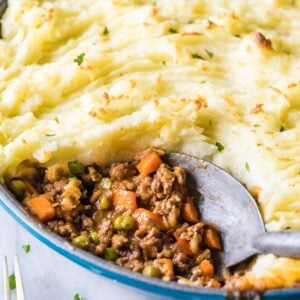 Close-up view of a spoon scooping out meat and veggies from a dish of shepherd's pie.