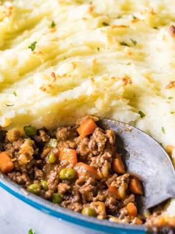 Close-up view of a spoon scooping out meat and veggies from a dish of shepherd's pie.