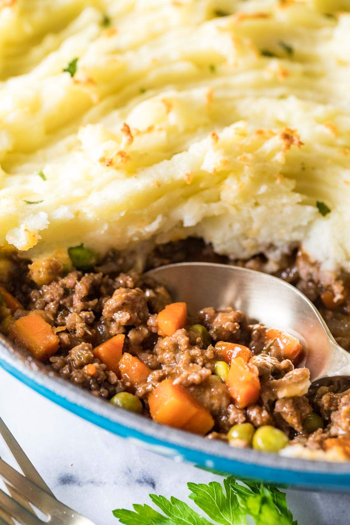 Spoon scooping ground meat and vegetables out from under a mashed potato topping.