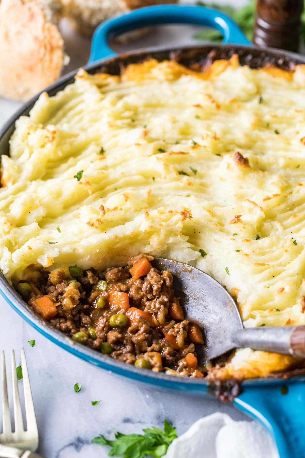 Close-up view of a spoon scooping out meat and veggies from a dish of shepherd's pie.