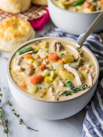 White bowl of chicken pot pie soup with mixed veggies and rotisserie chicken.