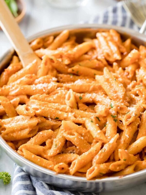 Wooden spoon resting in a large skillet of penne alla vodka topped with parmesan cheese.