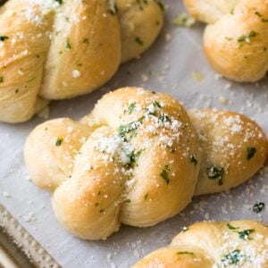 Homemade garlic knots topped with chopped fresh basil and grated parmesan after baking.