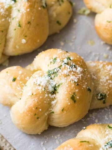 Homemade garlic knots topped with chopped fresh basil and grated parmesan after baking.