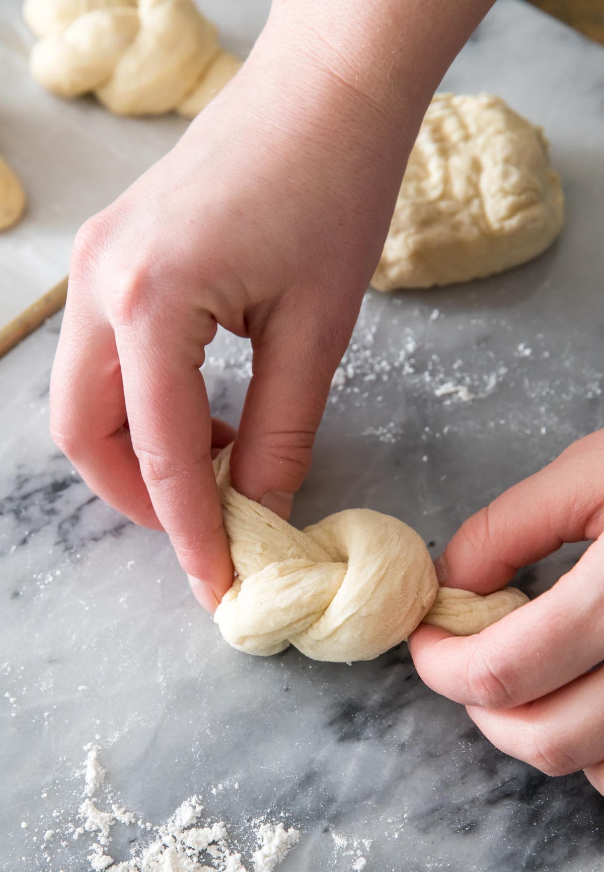 Hands twisting bread dough into a knot.