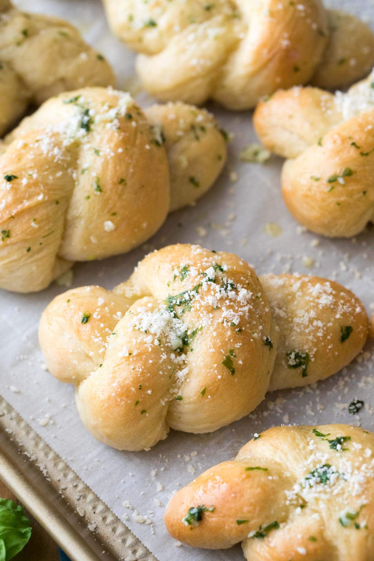 Homemade garlic knots topped with chopped fresh basil and grated parmesan after baking.