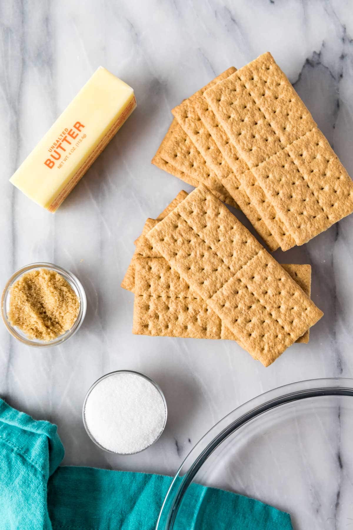 Overhead view of ingredients including graham cracker sheets, butter, brown sugar, and granulated sugar.