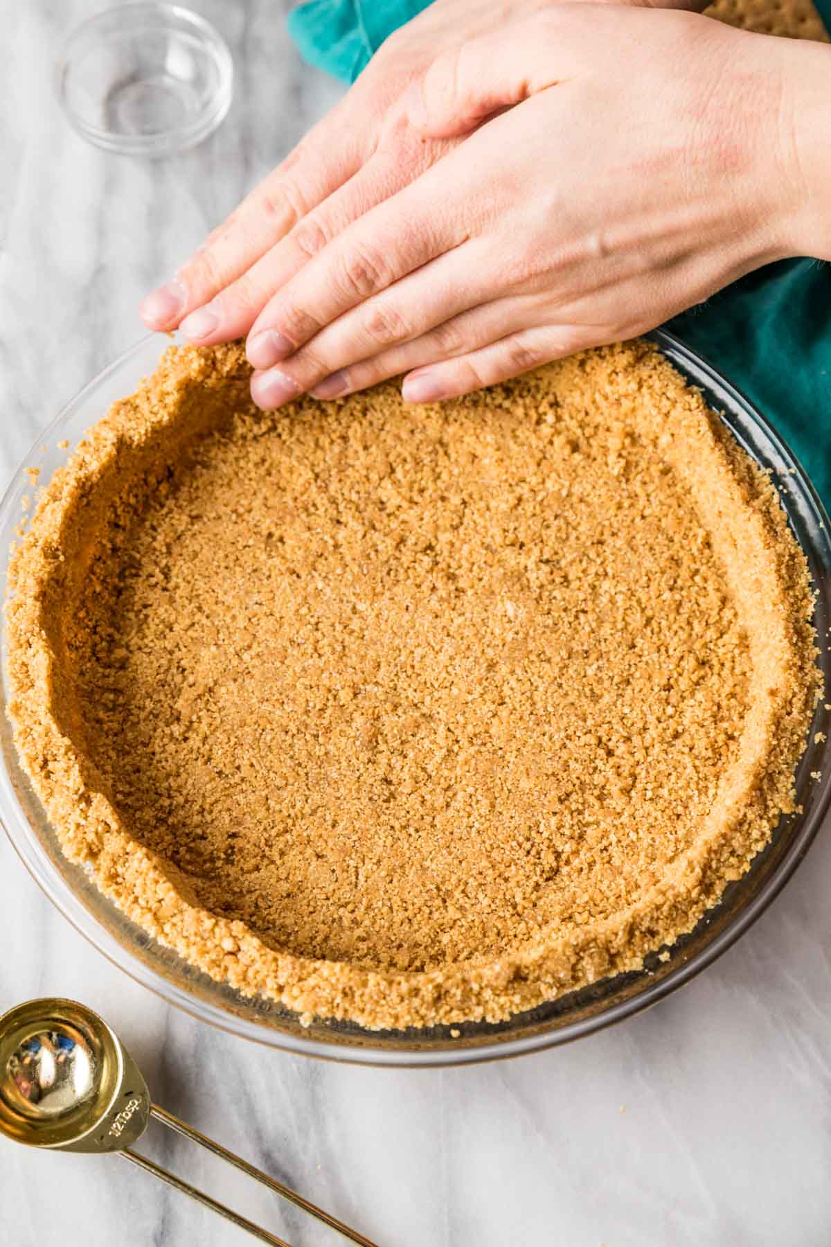 Pressing graham cracker crumbs into a glass pie plate.
