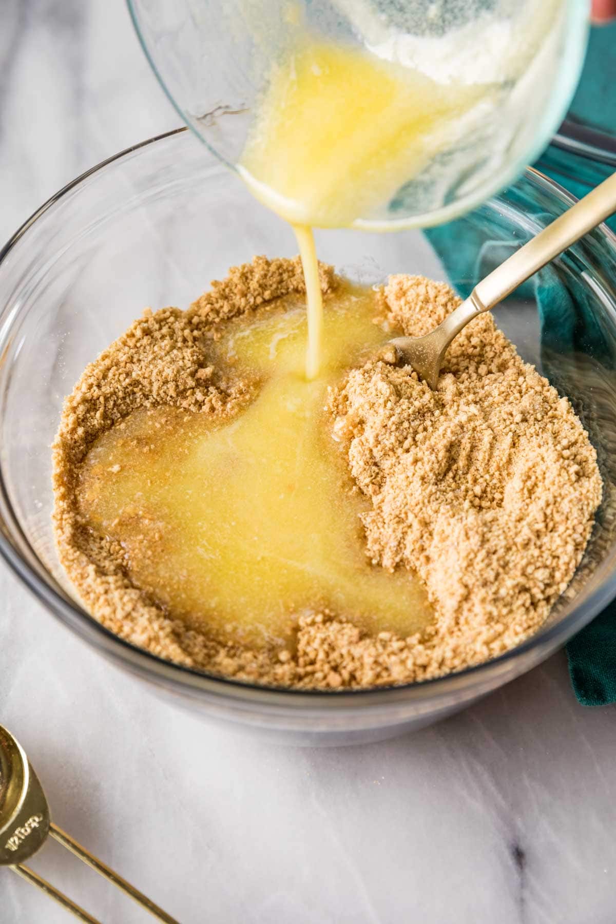 Melted butter being poured into graham cracker crumbs.