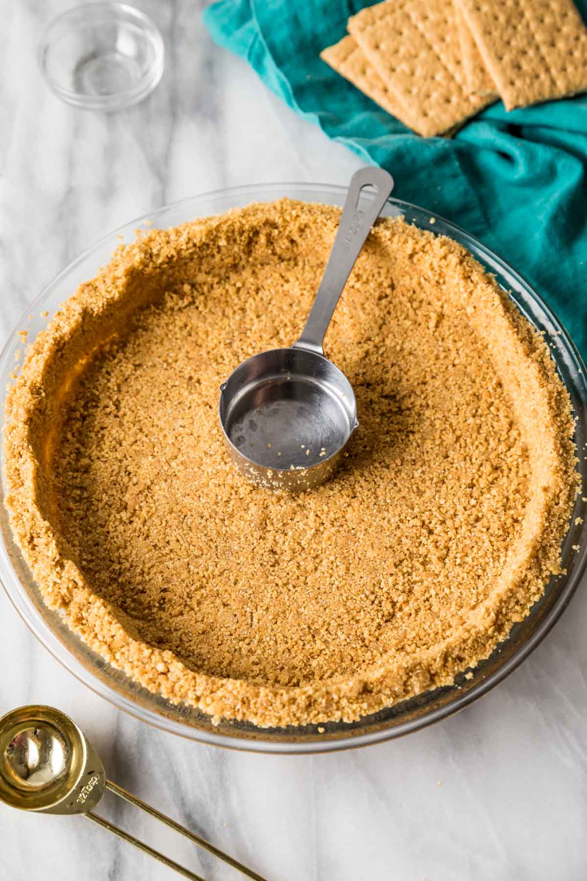 Metal measuring cup sitting inside a prepared graham cracker crust.