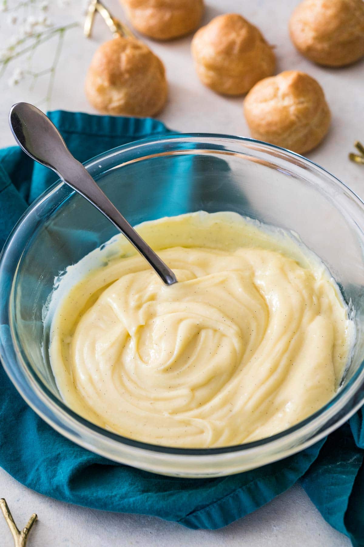 Bowl of pastry cream with choux buns in the background.