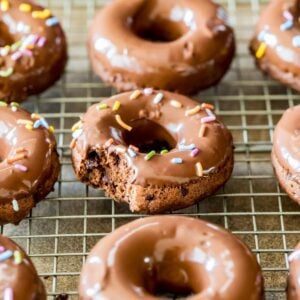 Chocolate donuts topped with chocolate glaze and sprinkles on a cooling rack.