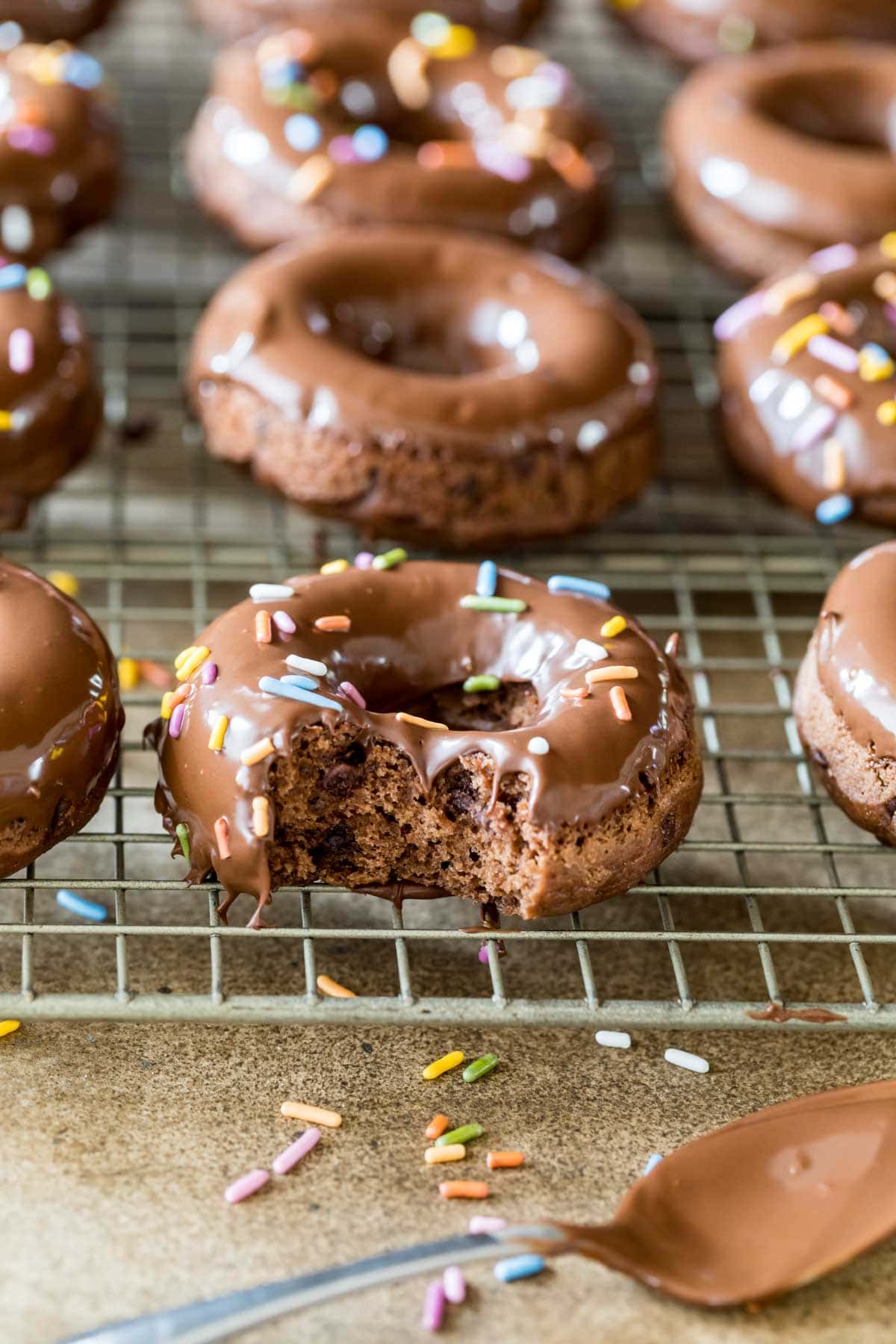 Donuts on a cooling rack with the closest one missing a bite.