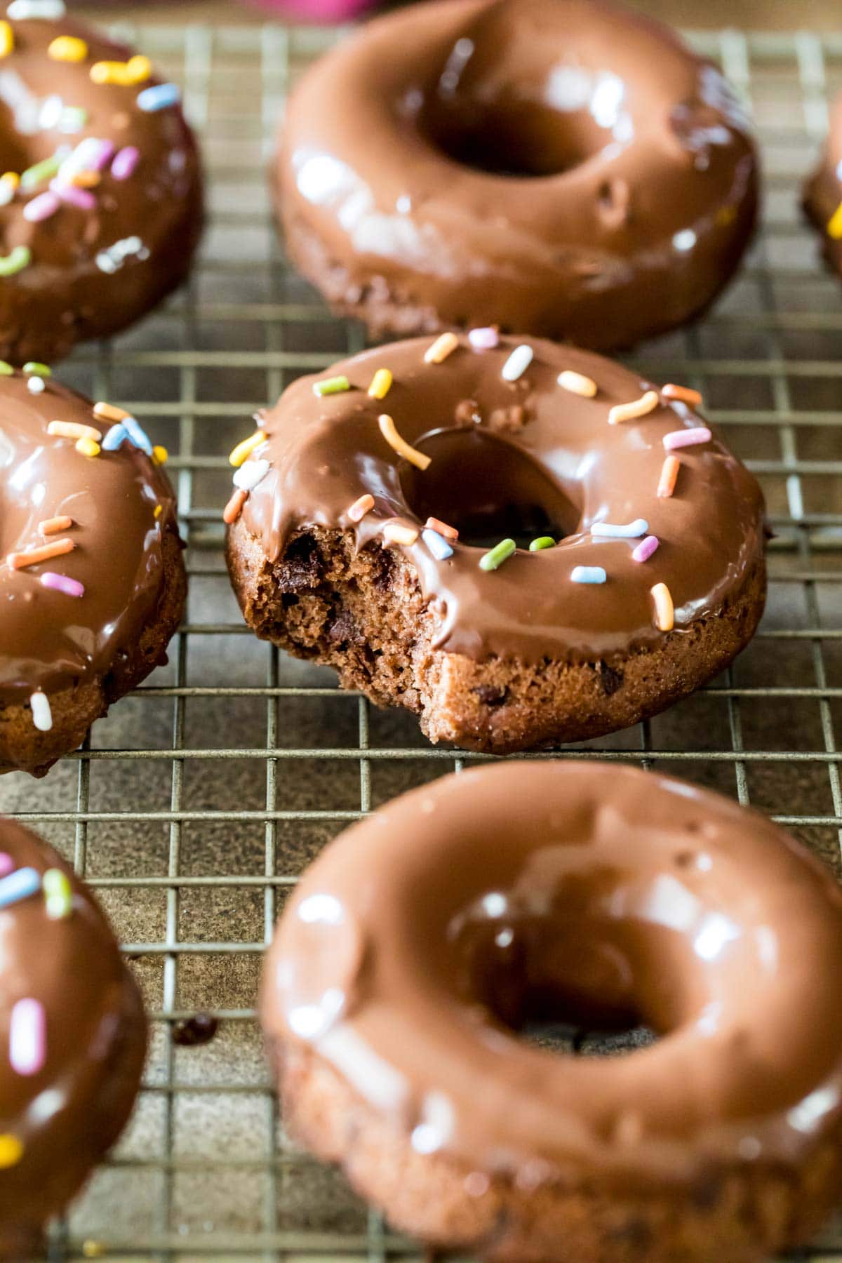 Chocolate donuts topped with chocolate glaze and sprinkles on a cooling rack.