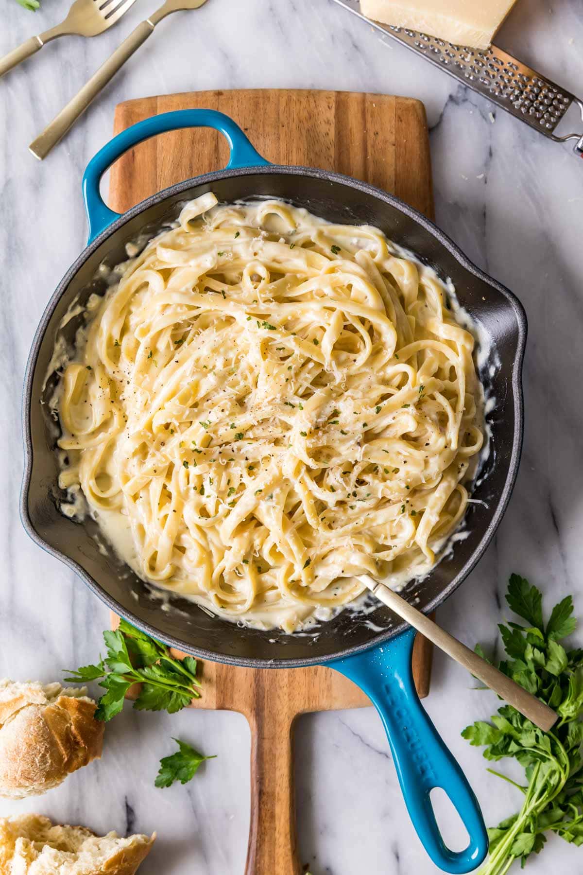 Overhead view of a skillet of fettuccine alfredo on a wood cutting board.