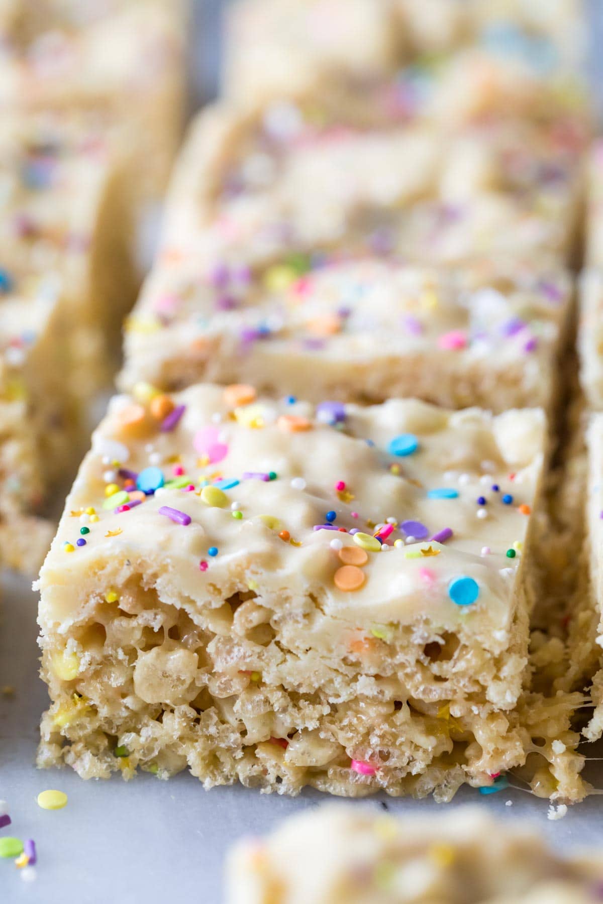 Close-up view of rice krispie treats topped with a fudgy cake batter frosting and rainbow sprinkles.