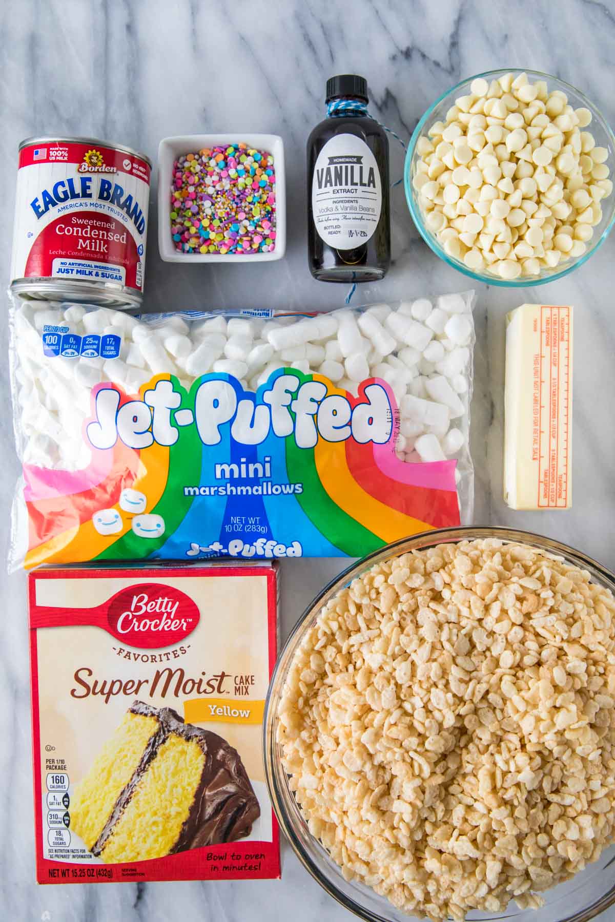 Overhead view of ingredients including rice krispies, marshmallows, sweetened condensed milk, cake mix, sprinkles, and more.