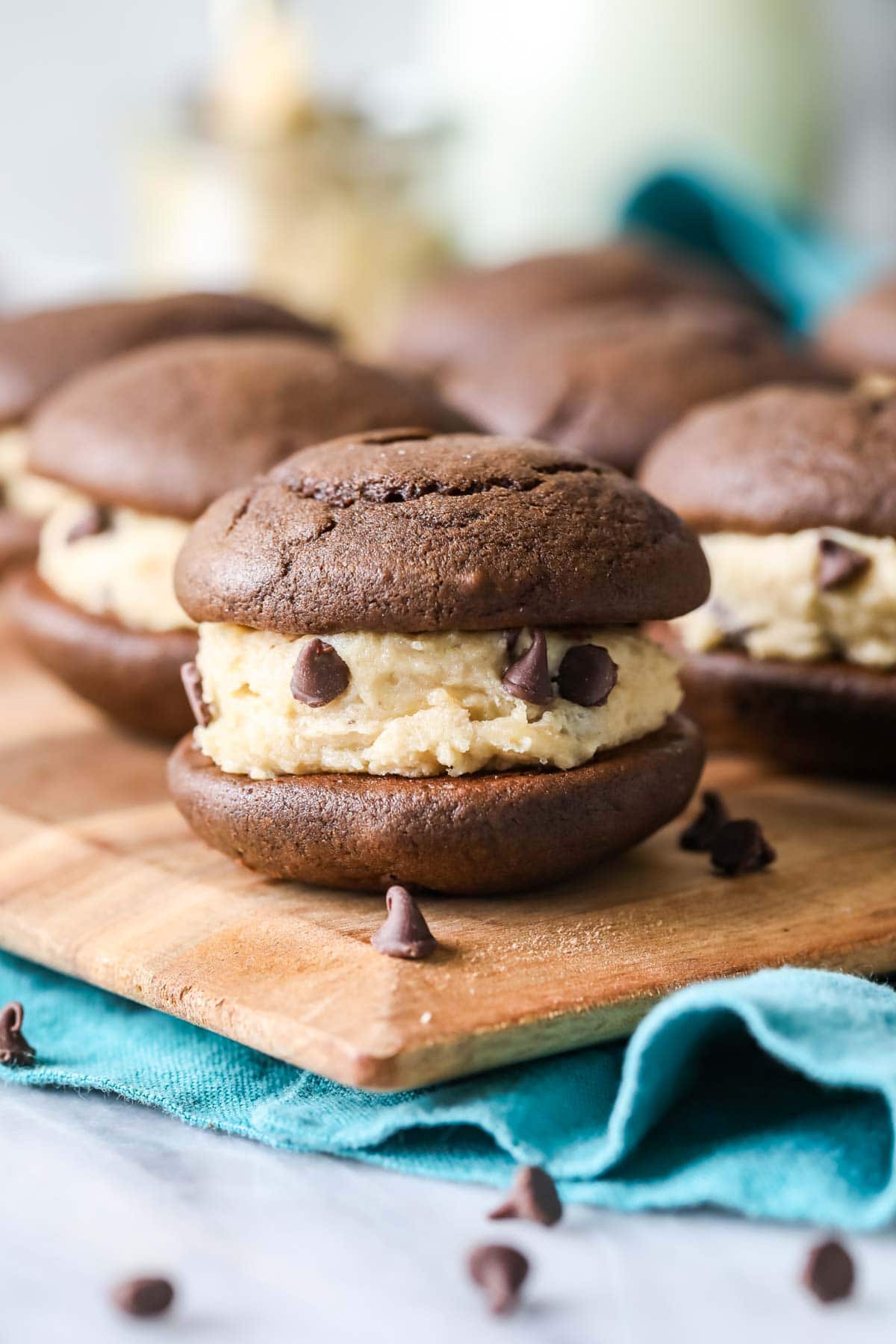 Close-up view of chocolate whoopie pies with a cookie dough filling on a wood cutting board.
