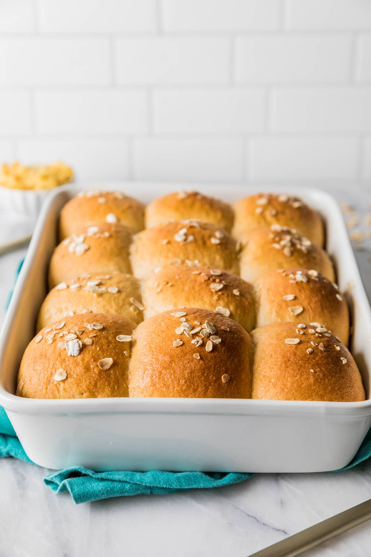 Head-on view of a baking pan of golden brown rolls made with wheat flour and an oat topping.