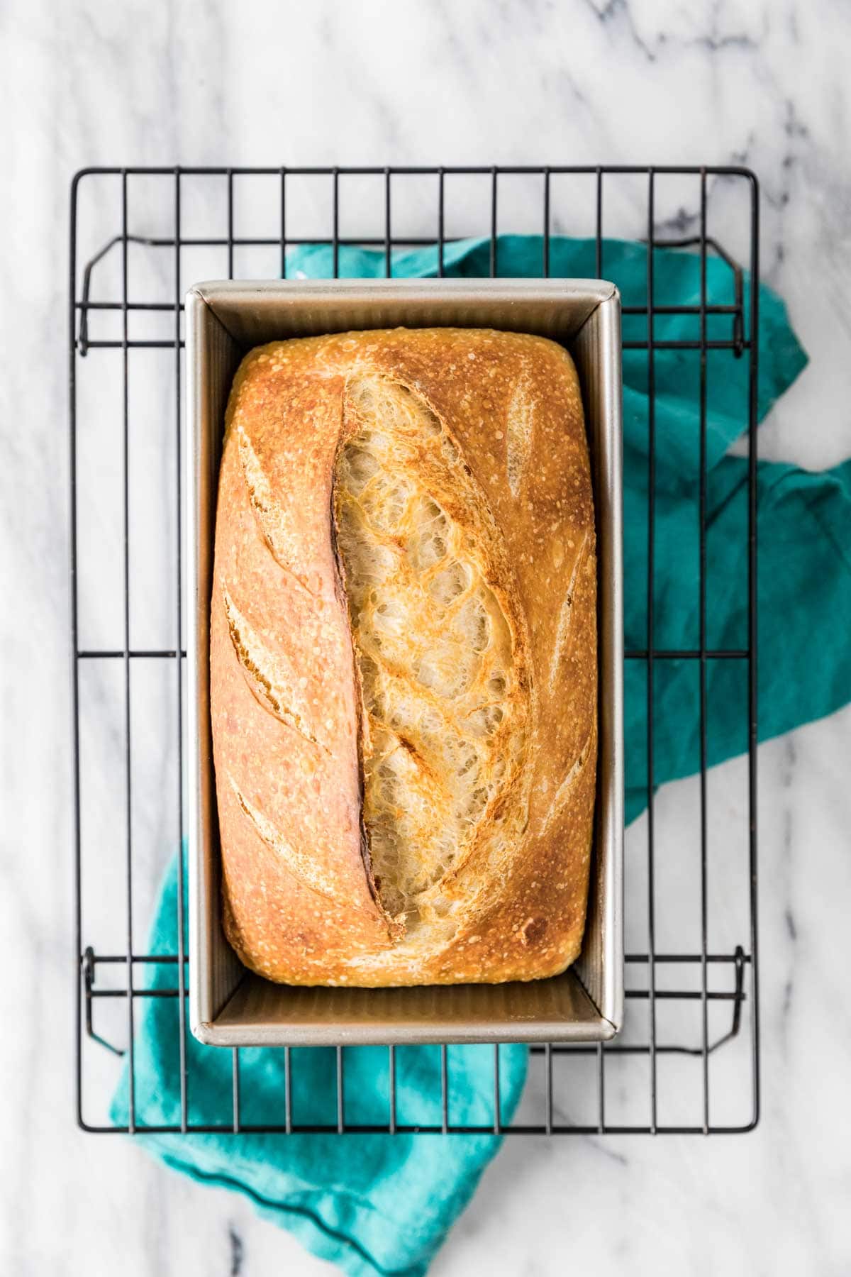 Overhead view of a loaf of homemade bread in a bread pan on a cooling rack.