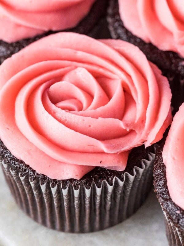 Piped rosettes of raspberry buttercream frosting on top of chocolate cupcakes.