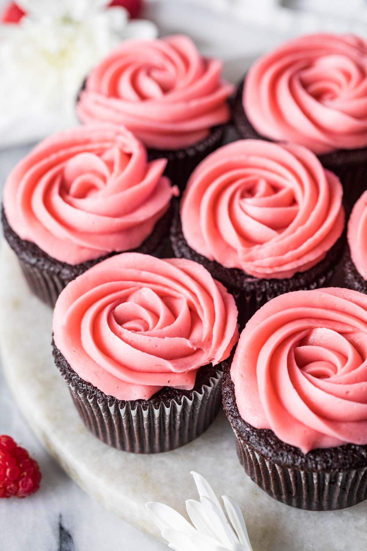 Piped rosettes of raspberry buttercream frosting on top of chocolate cupcakes.