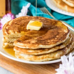 Sirup wird über einen mit Butter bestrichenen Stapel Sauerteigpfannkuchen gegossen.