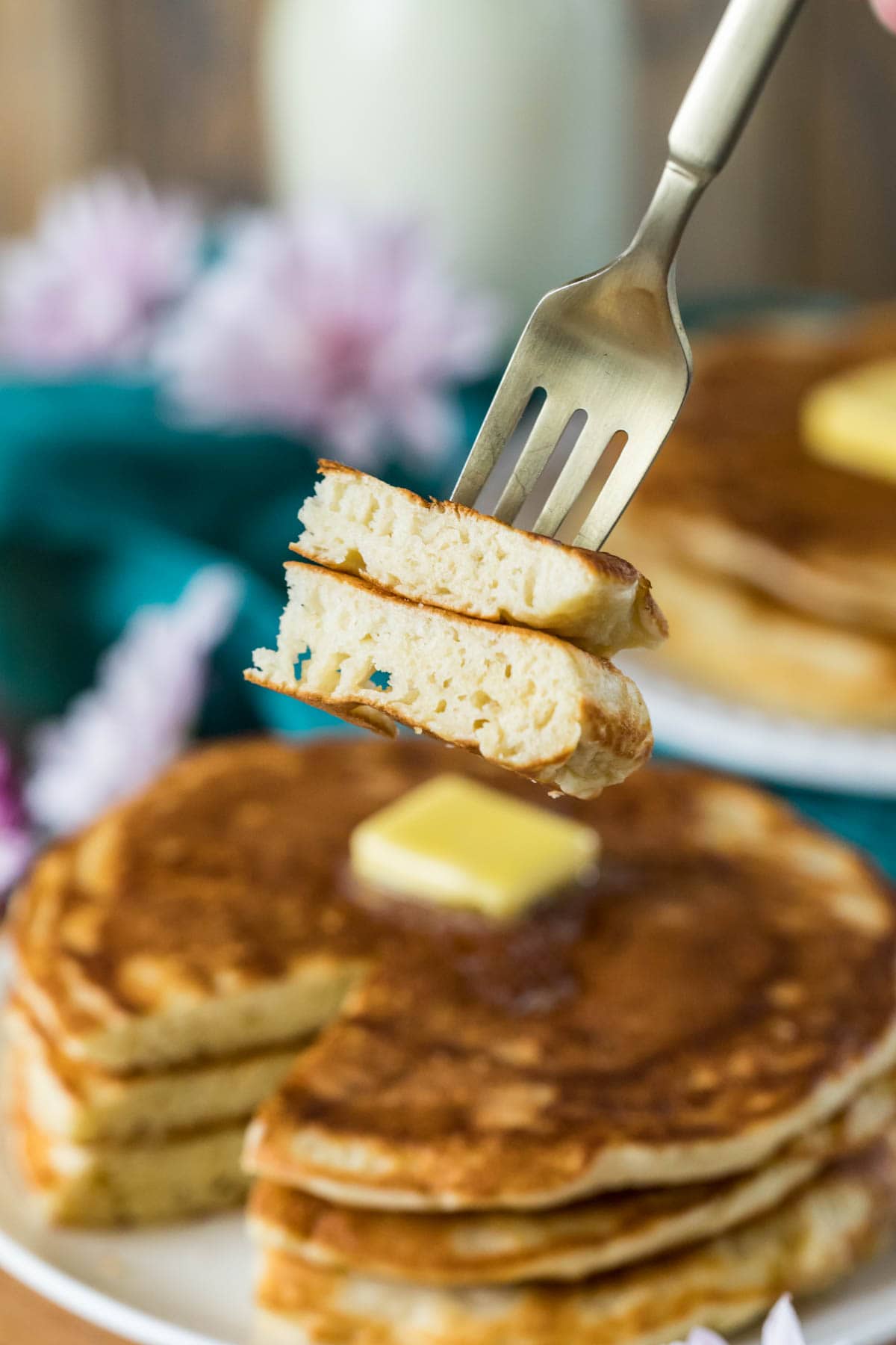 Fork with a bite of pancakes taken from a tall stack of buttered pancakes in the background.