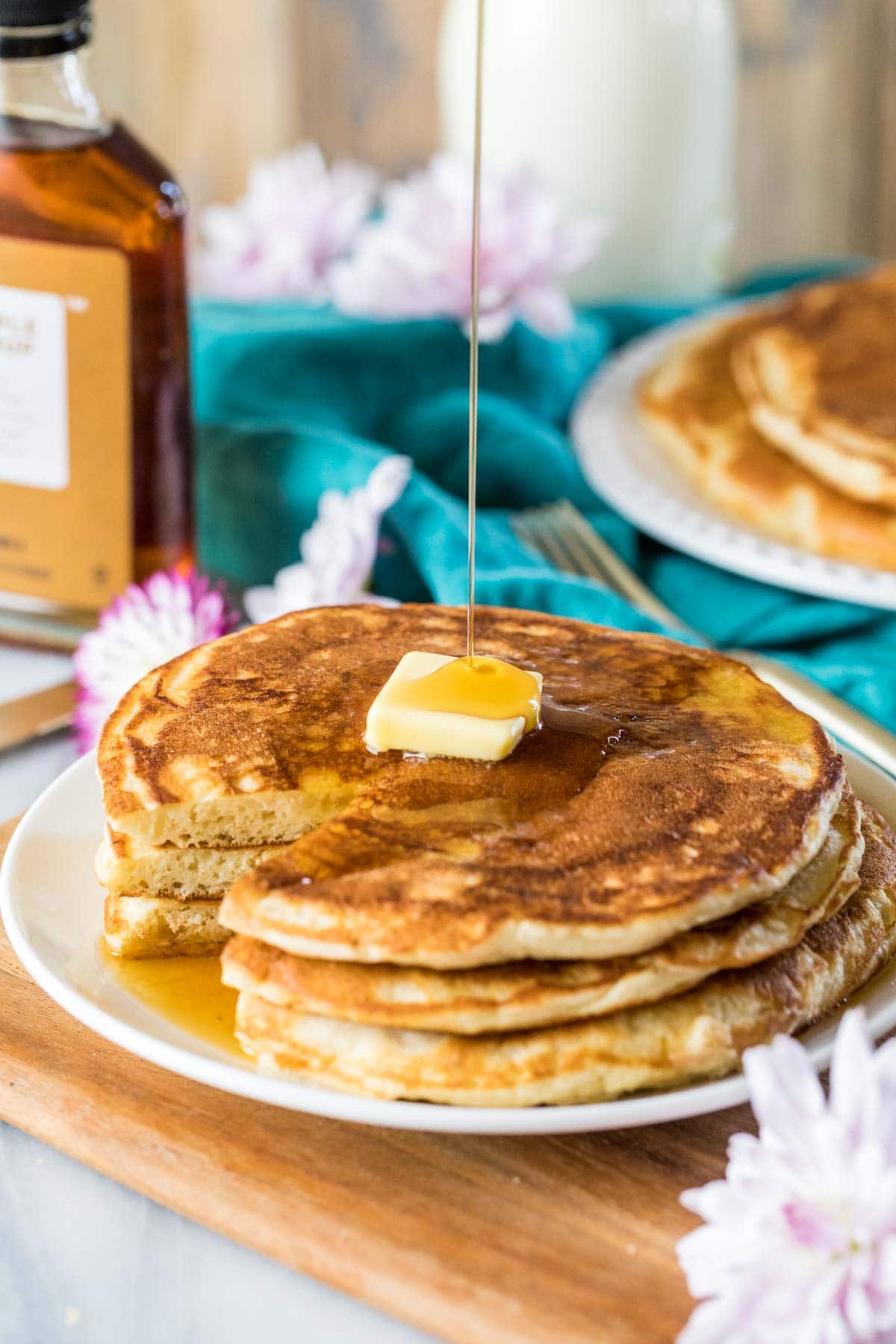 Syrup being poured over a buttered stack of sourdough pancakes.