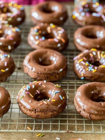 Close-up view of chocolate cake donuts topped with chocolate glaze and sprinkles on a metal cooling rack.