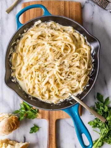 Overhead view of a skillet of fettuccine alfredo on a wood cutting board.