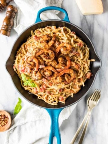 Overhead view of a skillet of pasta topped with seasoned shrimp.