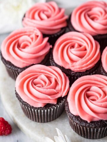 Piped rosettes of raspberry buttercream frosting on top of chocolate cupcakes.
