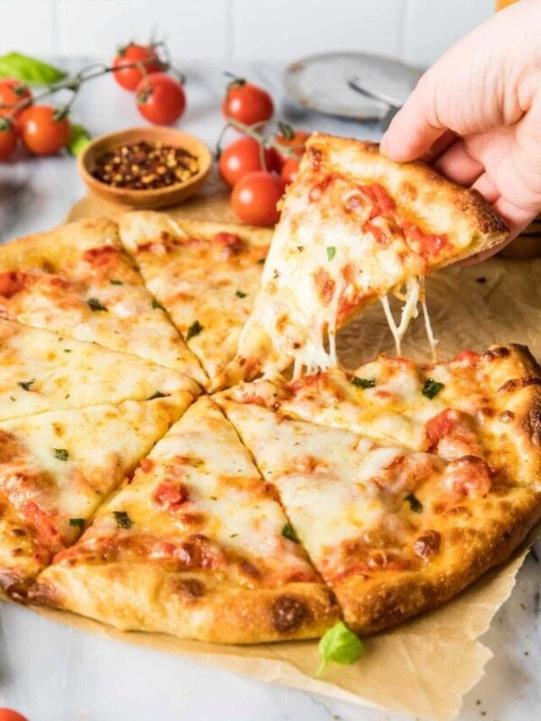 Hand pulling a slice of cheesy pizza made with a sourdough pizza crust.