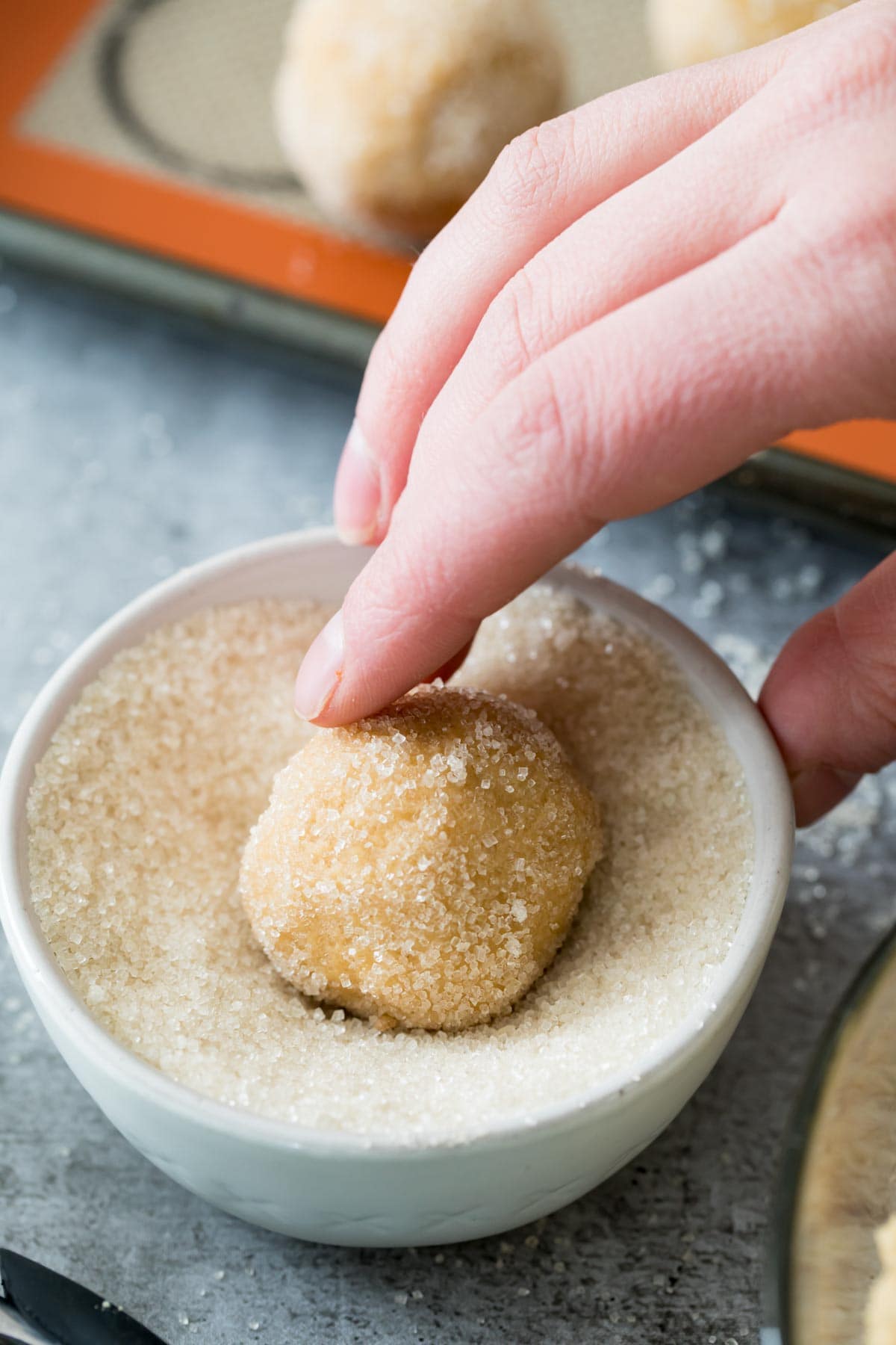 Cookie dough ball being rolled in granulated sugar.