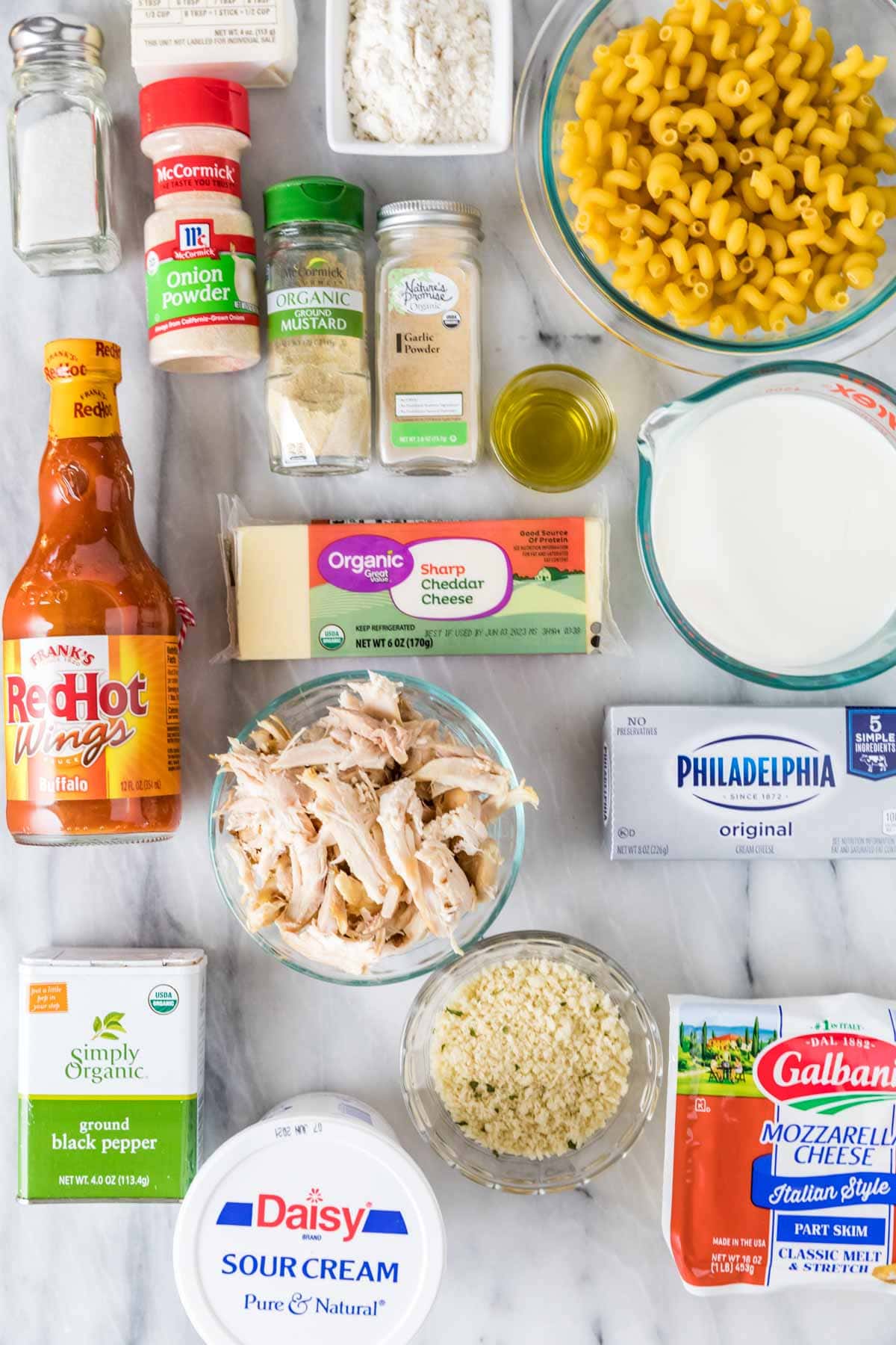 Overhead view of ingredients including buffalo sauce, shredded chicken, macaroni noodles, and more.