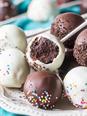 White and dark chocolate coated chocolate cake pops on a plate, with the middle pop missing a bite.