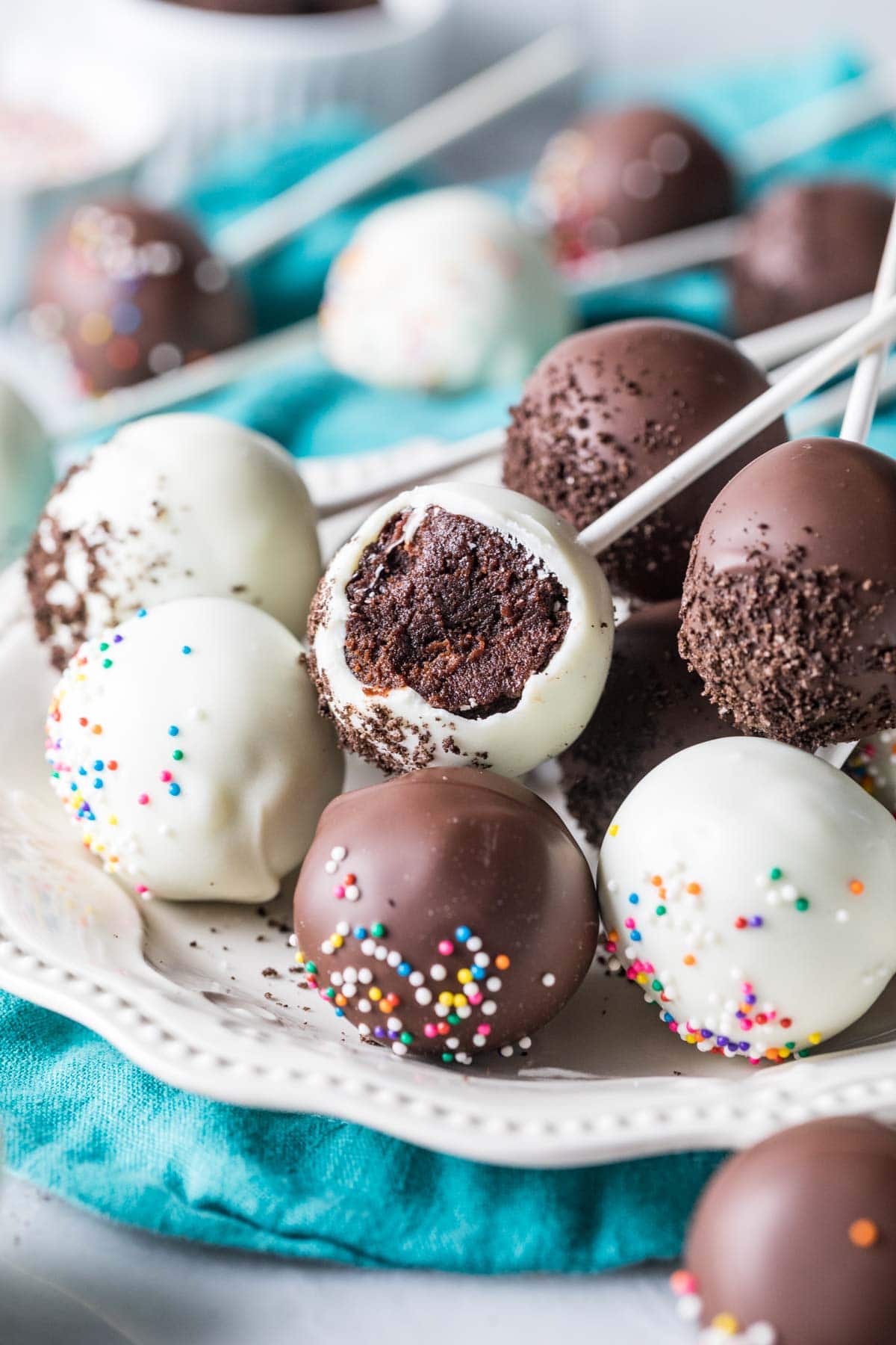 White and dark chocolate coated chocolate cake pops on a plate, with the middle pop missing a bite.