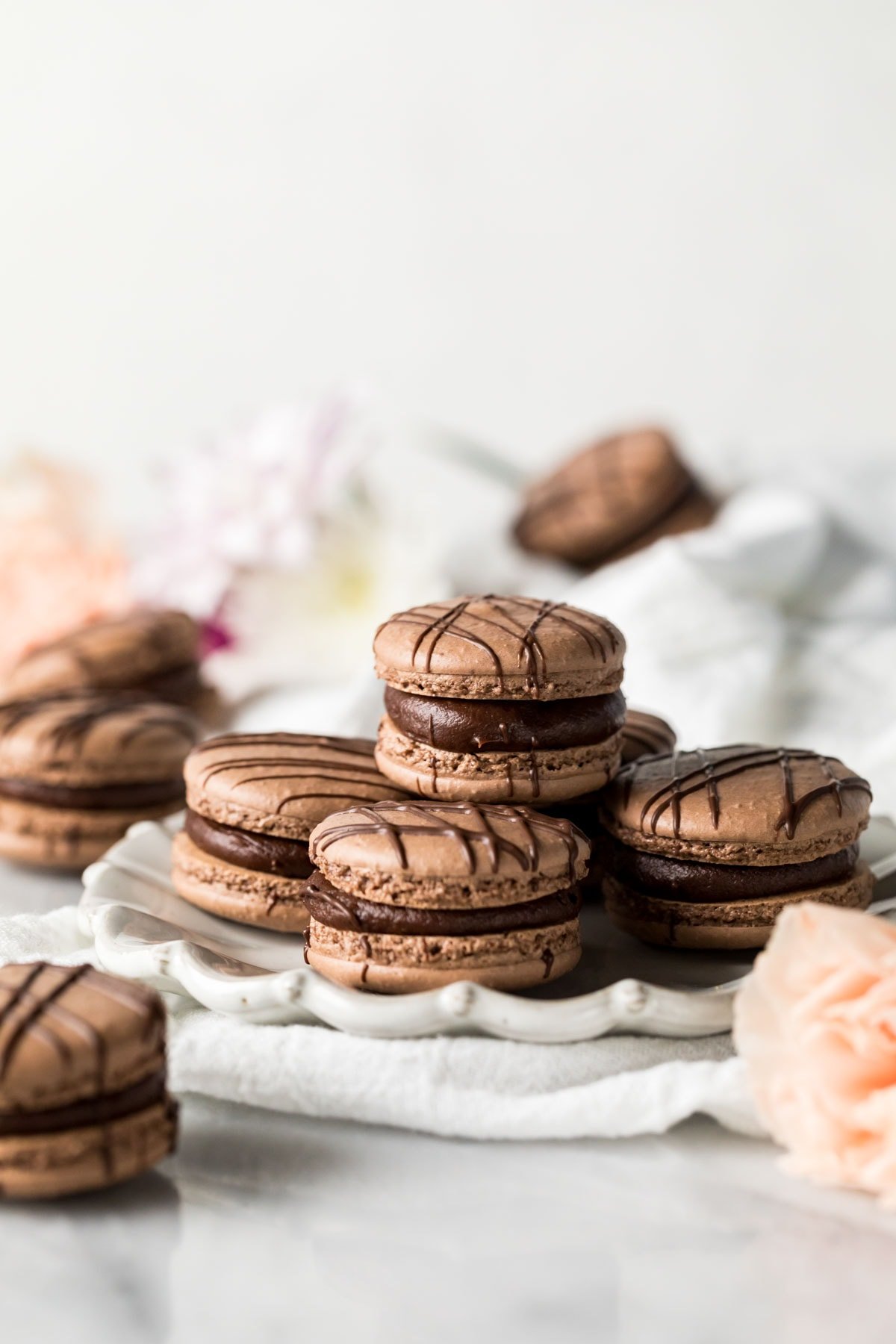 White plate with brown, ganache-filled macarons stacked on top of it.