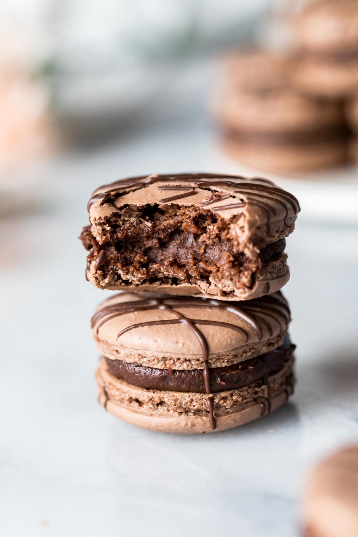 Two chocolate macarons stacked on top of each other with the top macaron missing a bite.