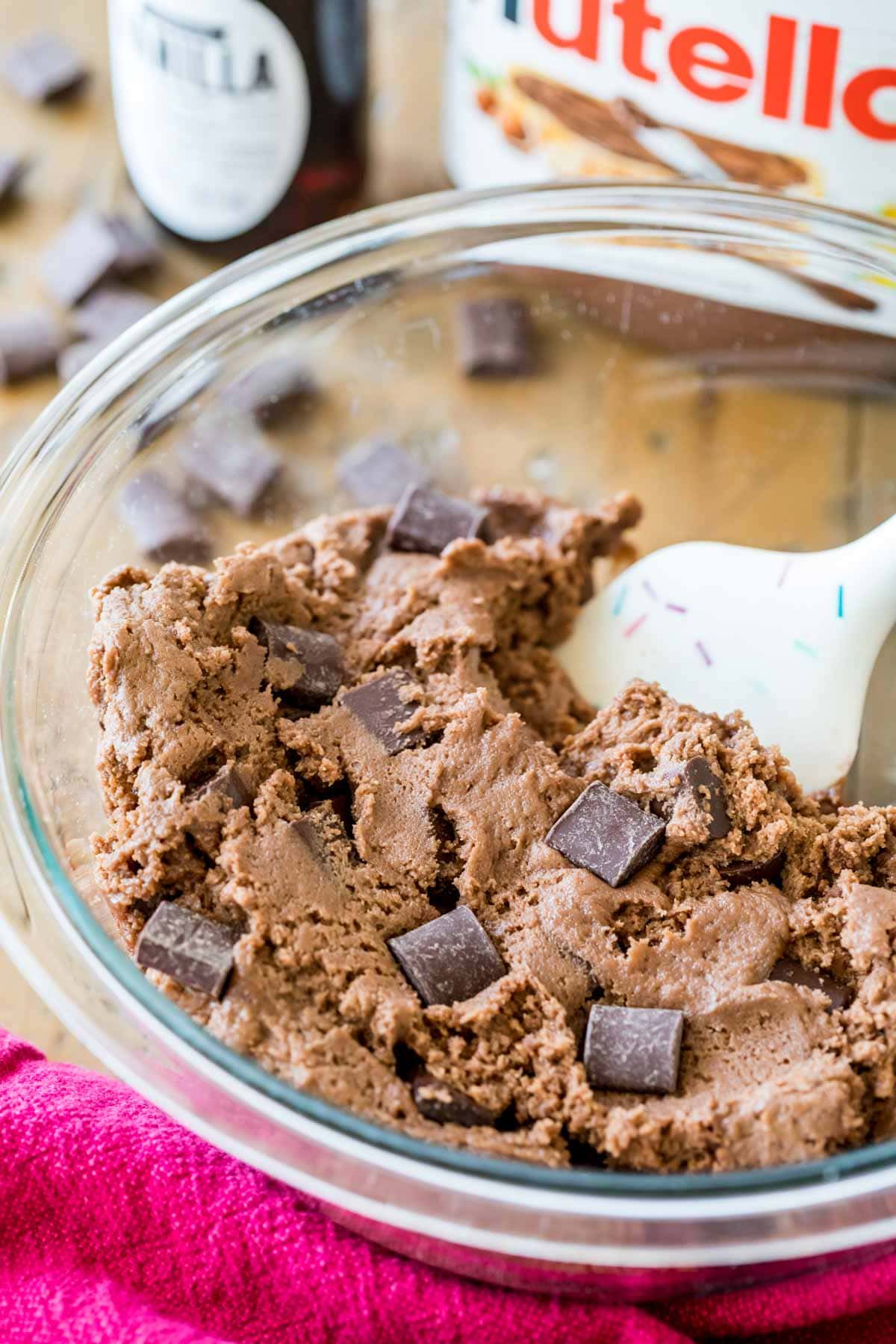 Spatula stirring a bowl of chocolate cookie dough studded with chocolate chunks.