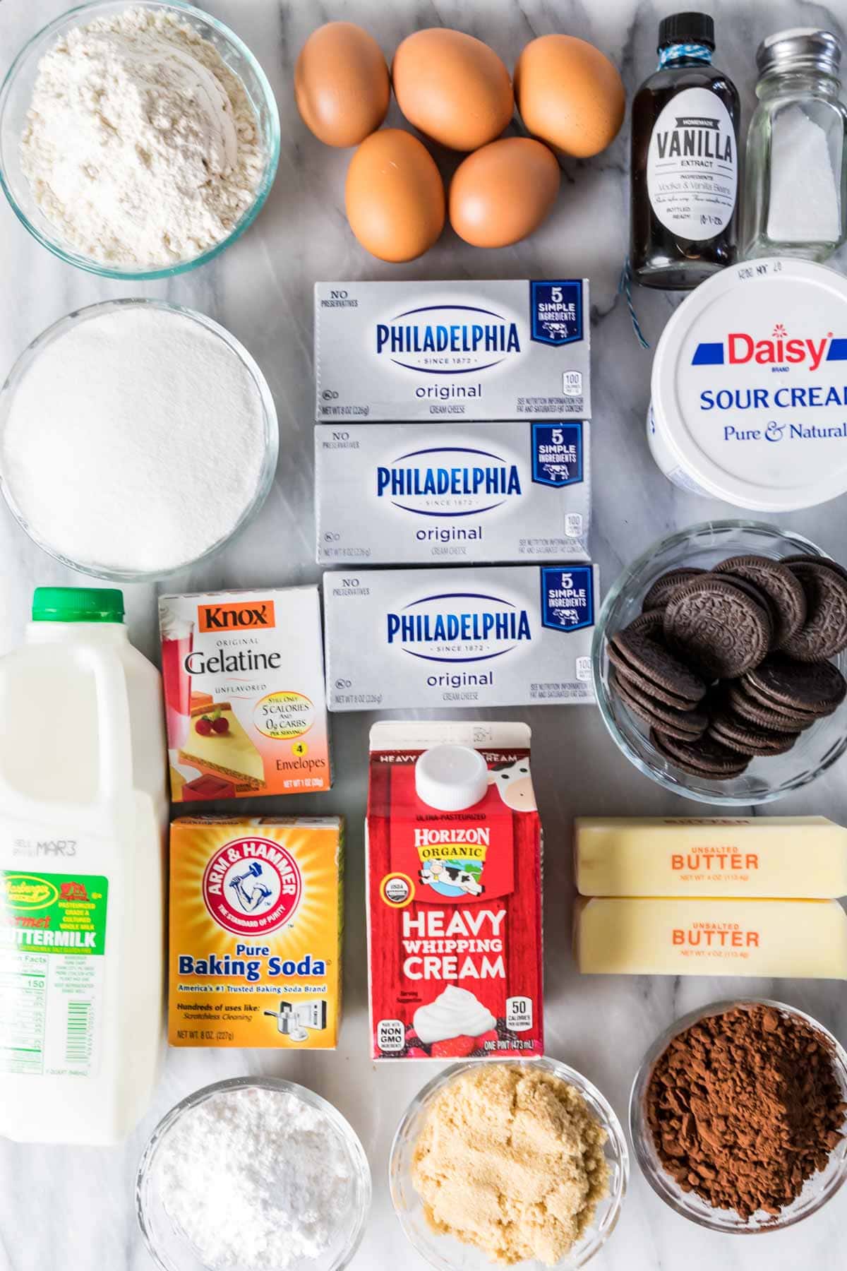 Overhead view of ingredients including eggs, flour, sour cream, cream cheese, oreos, and more.